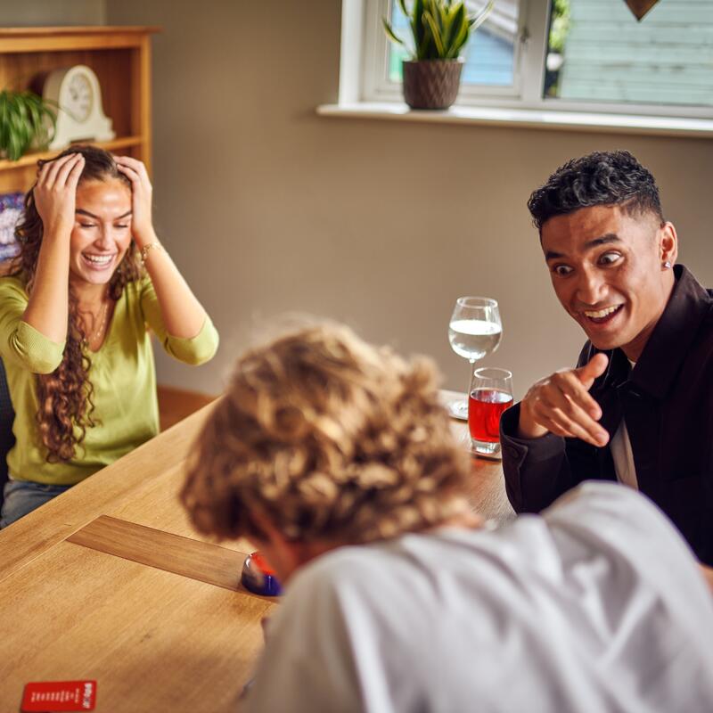 Friends sat around table playing Buzzed Out describing game